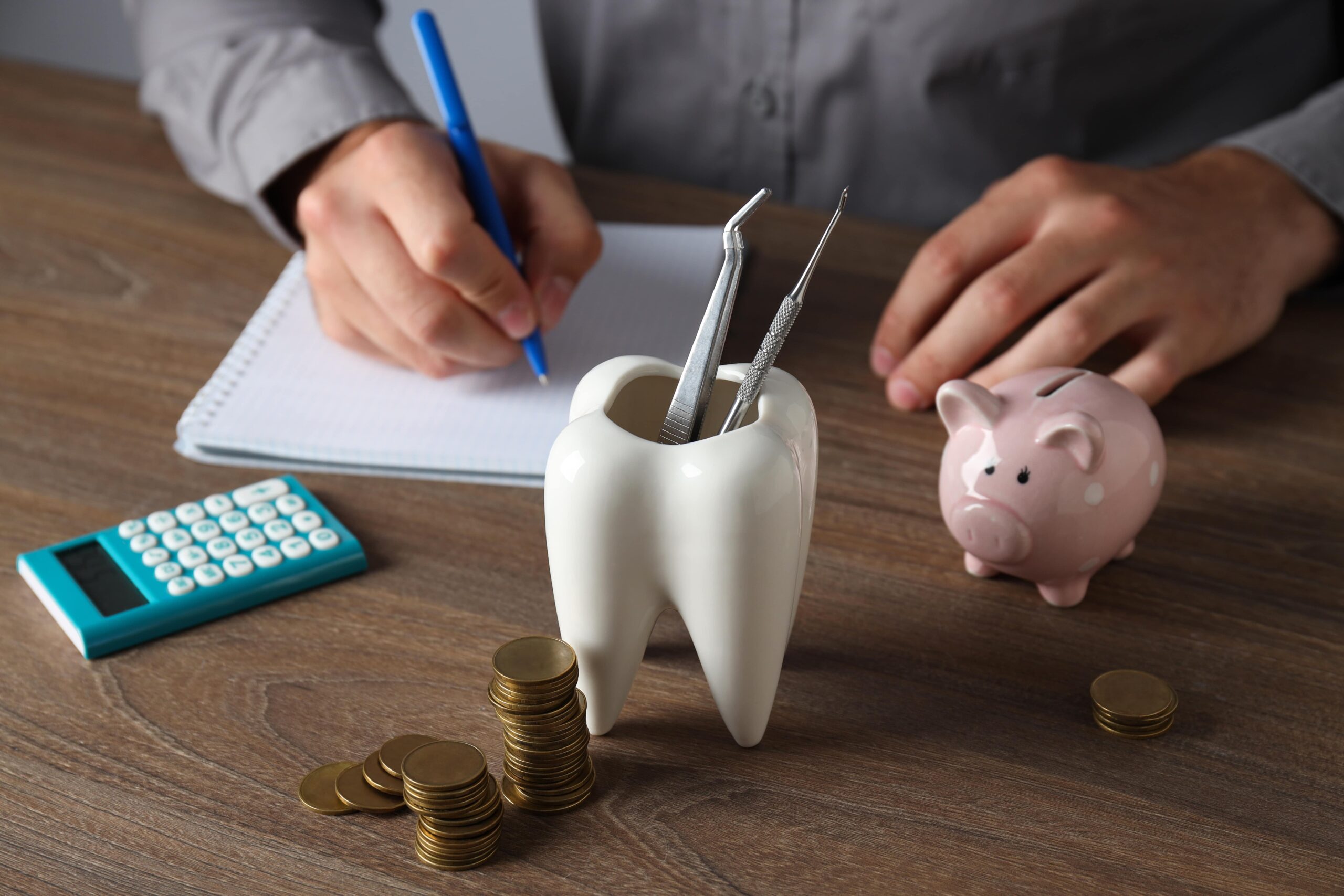 Tooth with dental instruments, piggy bank, calculator, coins and hands on table