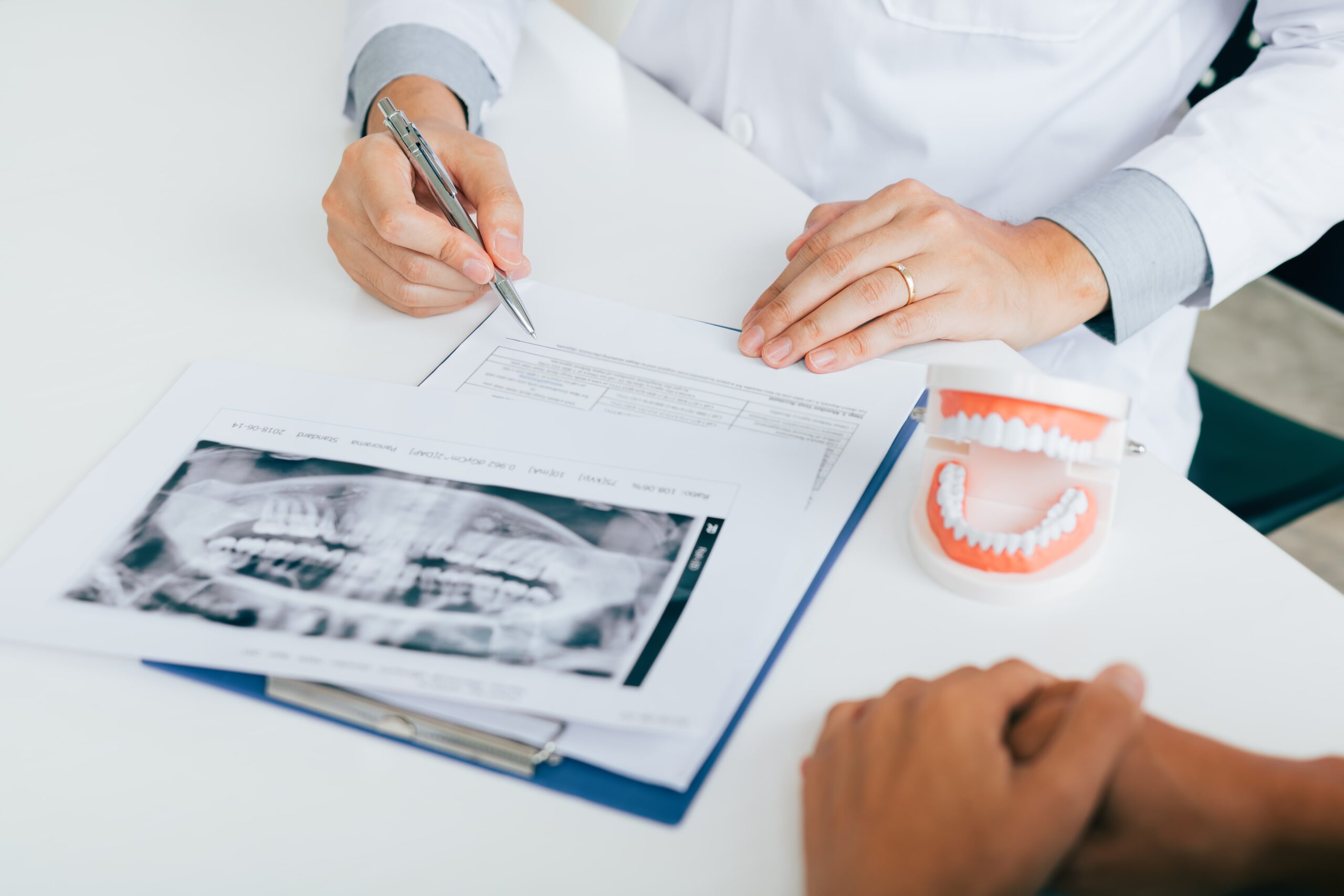 Dentist hand holding pen pointing x-ray picture and talking to the patient about medication.