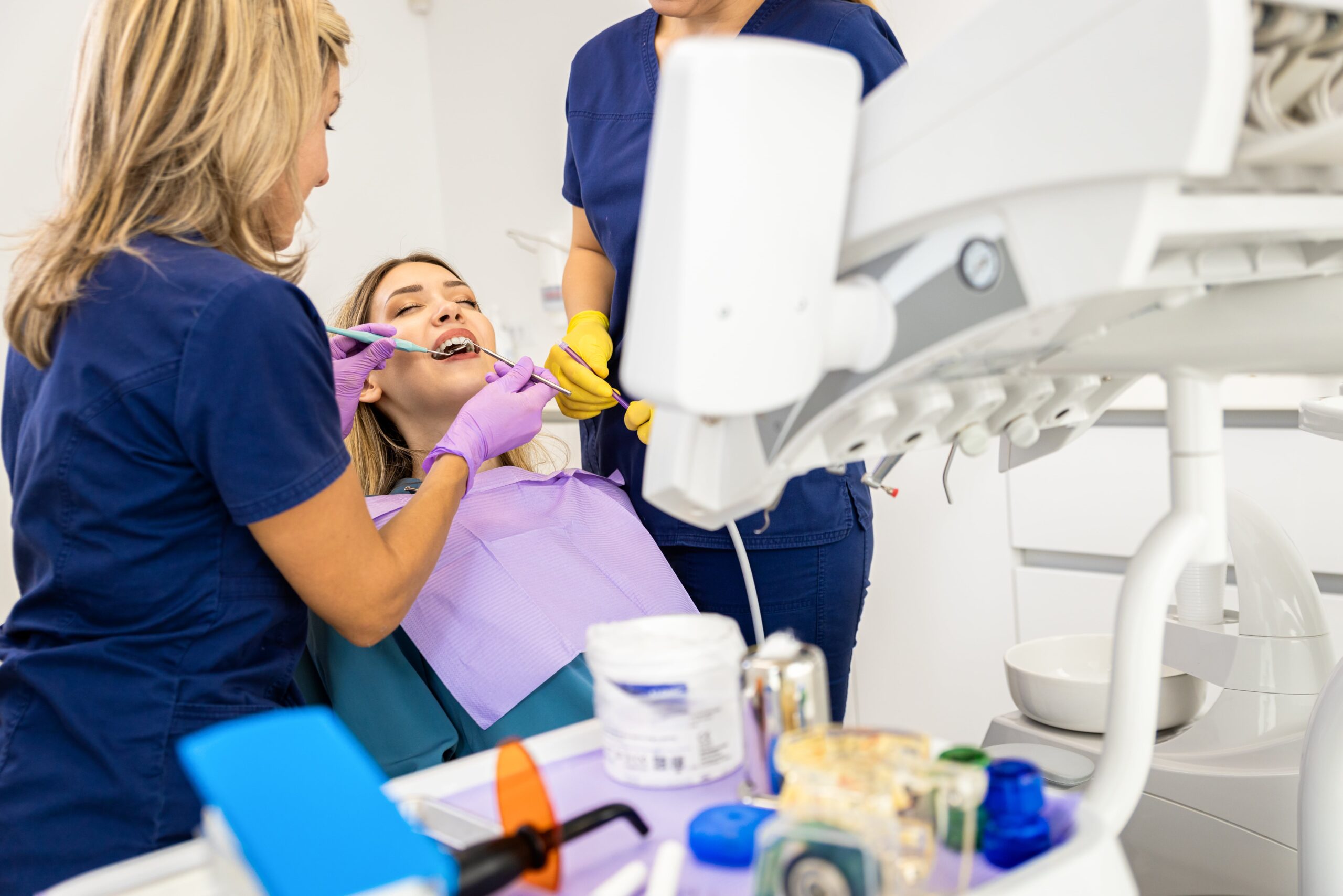 Female dentist with assistant working in dental clinic examining patient teeth.