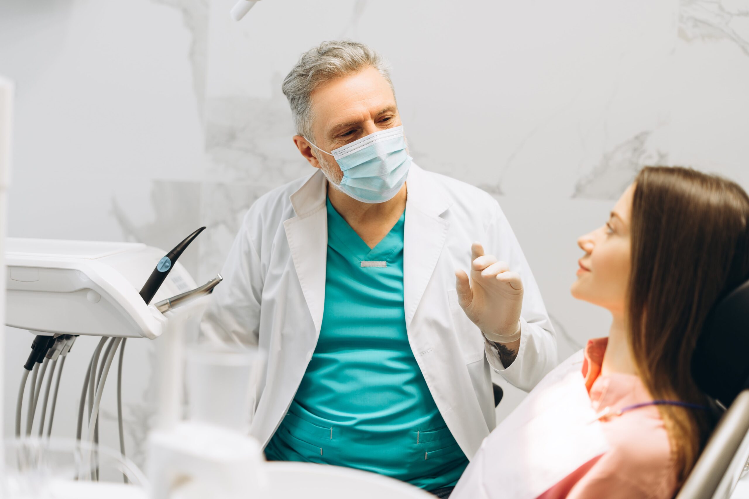 Mature friendly male dentist starting a consultation for young woman in his office