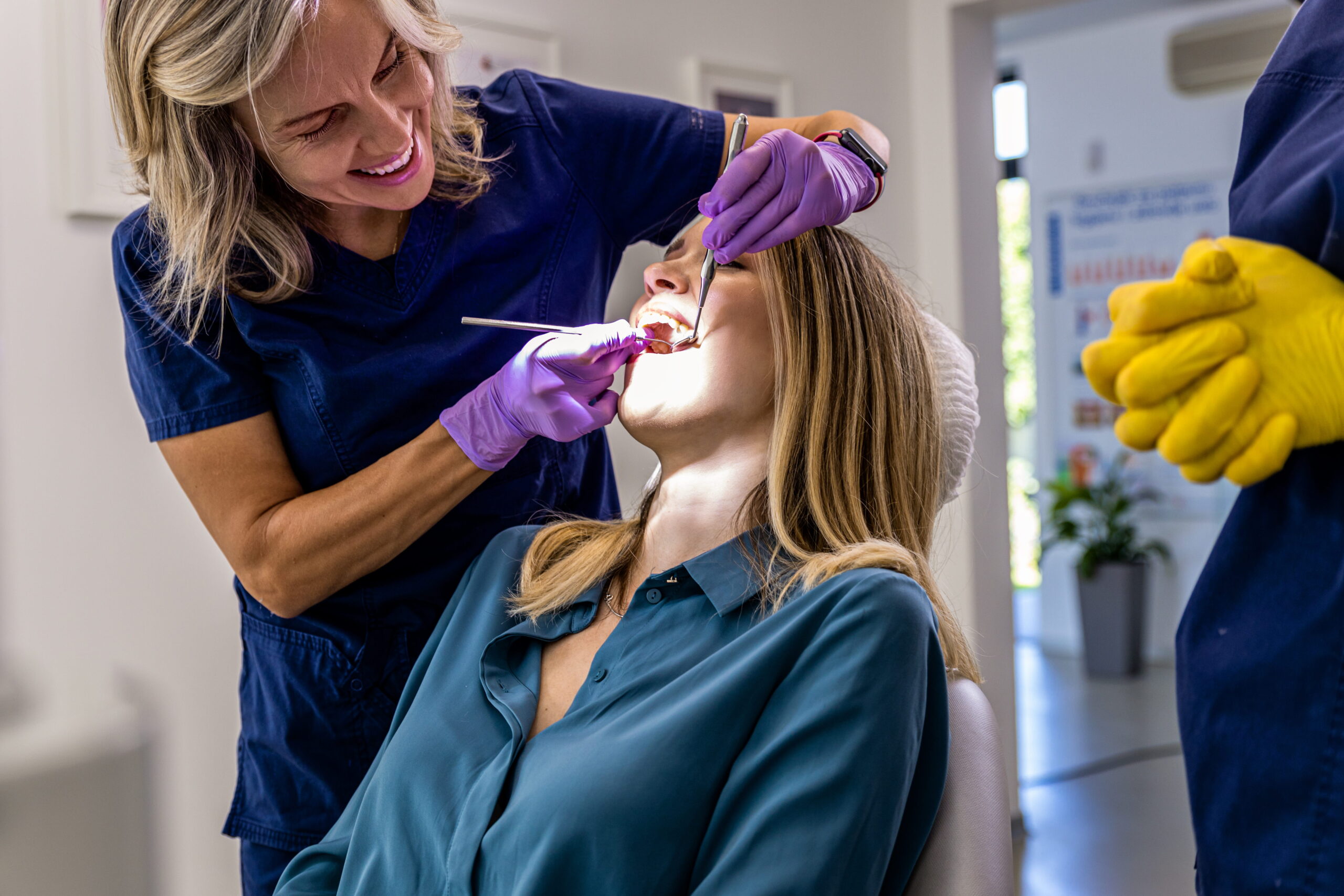 Female dentist with assistant working in dental clinic examining patient teeth.